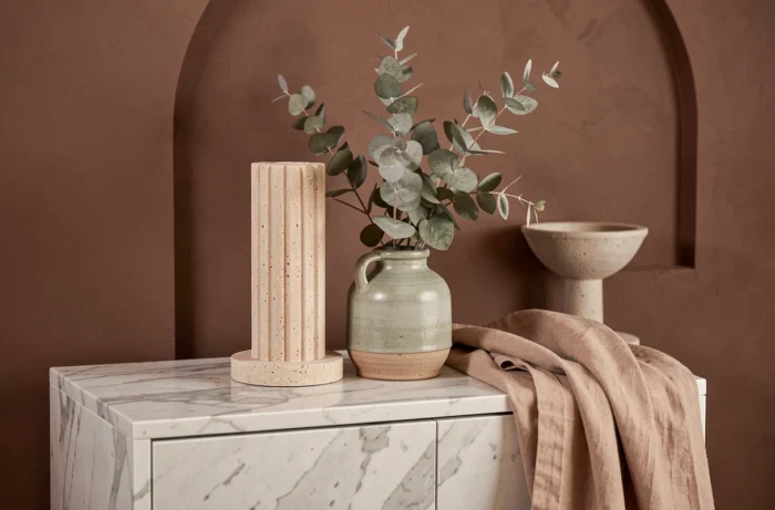 Vignette déco tendance sur un buffet en marbre avec bougeoir en travertin, vase en grès artisanal et jeté en lin beige contre un mur ocre argile